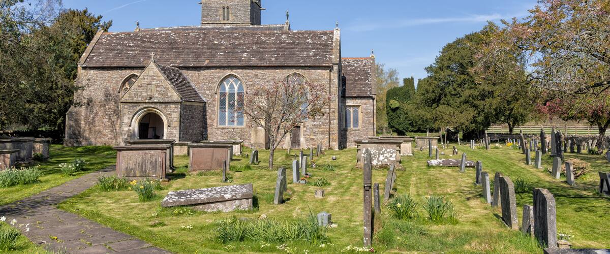 Una iglesia histórica con fachada de piedra, un campanario y un cementerio con lápidas.