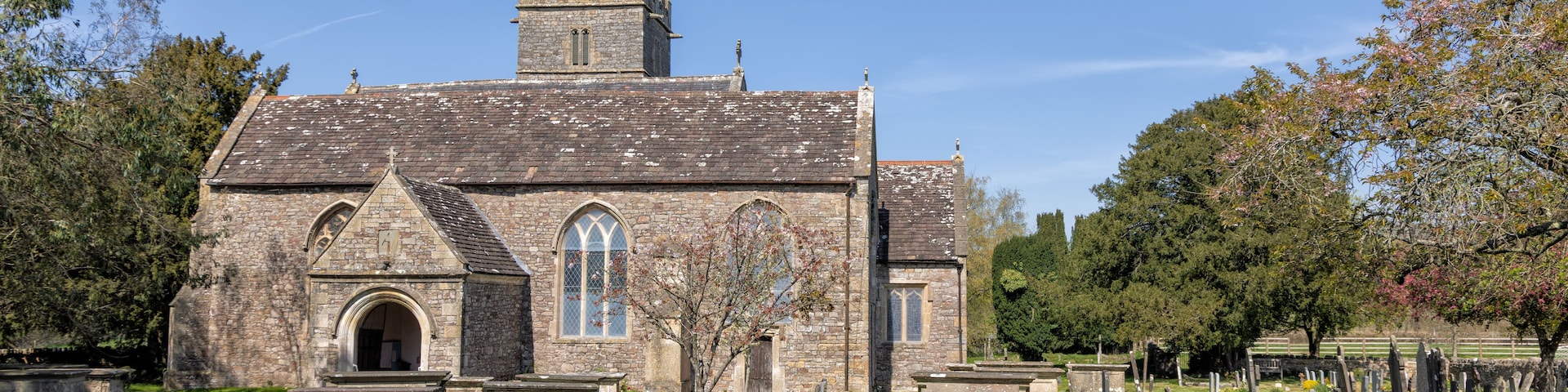 Uma igreja histórica com fachada de pedra, um campanário e um cemitério com lápides.