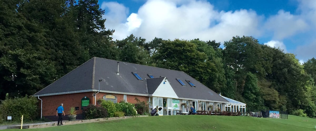 A clubhouse with a green roof, surrounded by a golf course and trees.