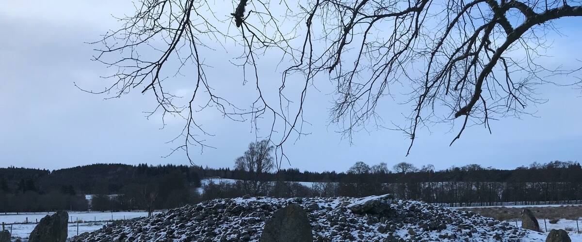 A snowy landscape with standing stones and a forest in the background.