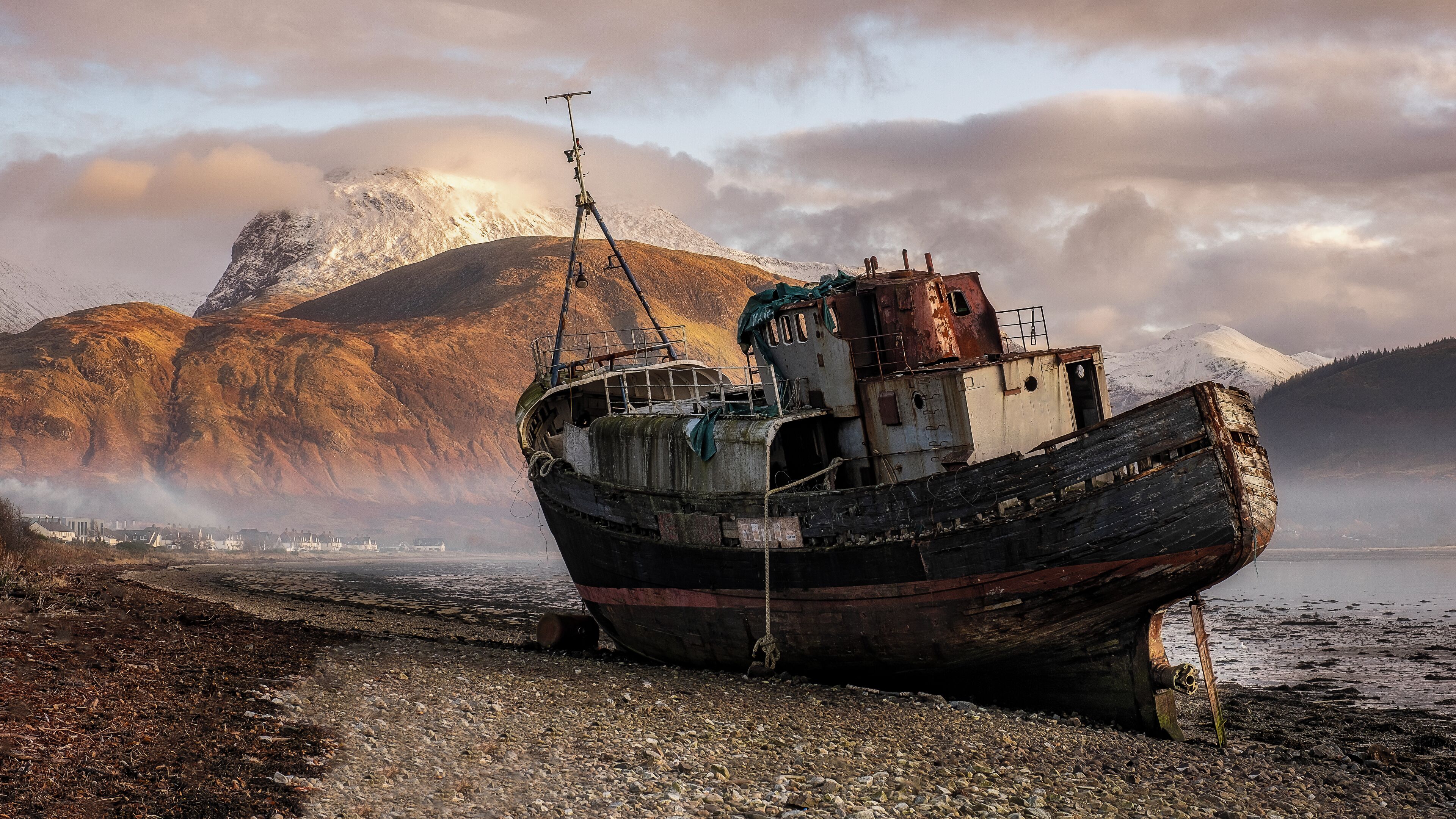 A weathered boat stranded on a rocky shore with mountains in the background.