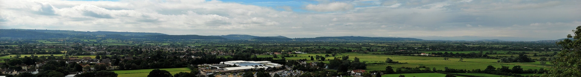 A rural landscape with rolling hills, a large building with a flat roof, and scattered houses.