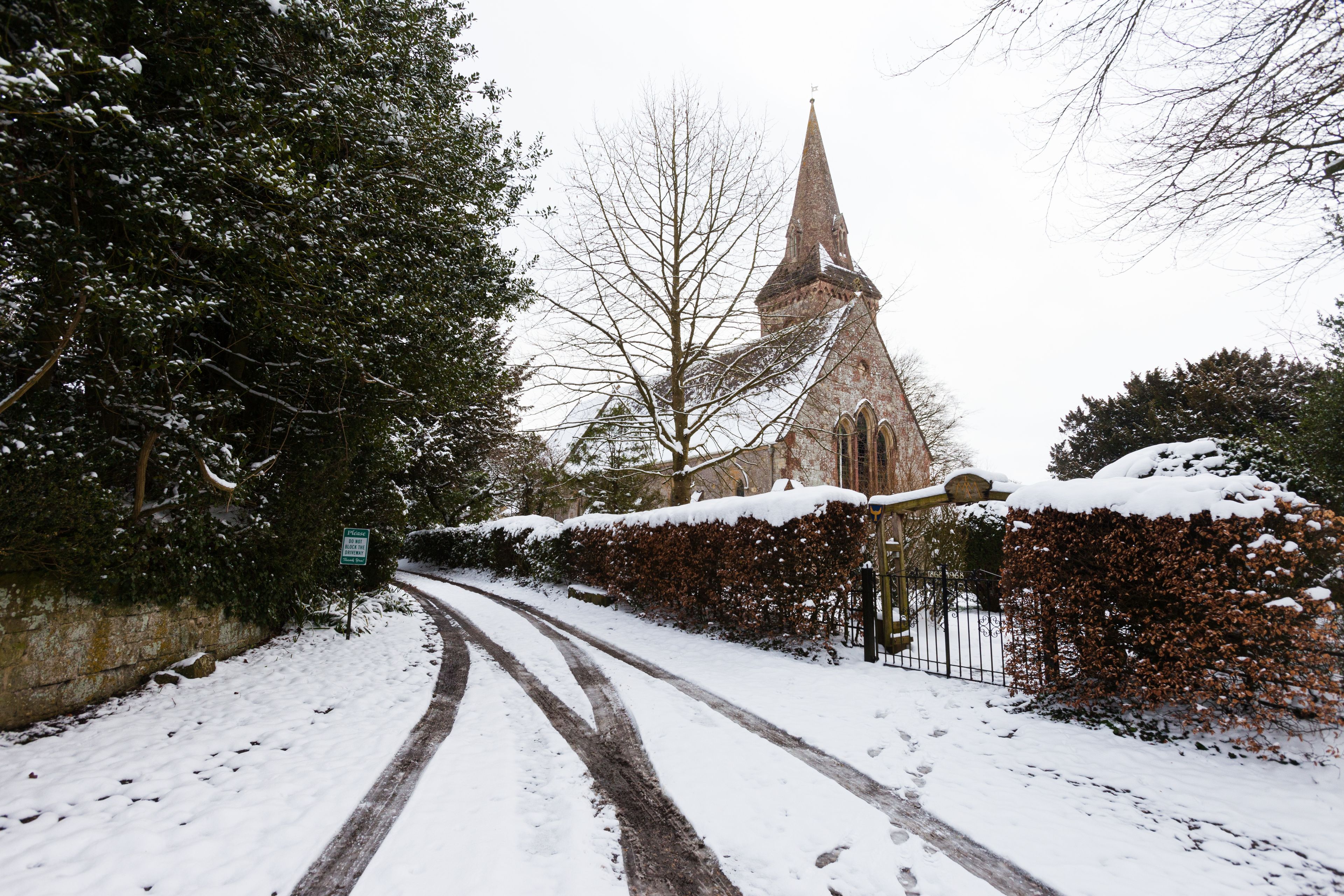 A snow-covered church with a tall spire, a paved road, and a hedge along the side.