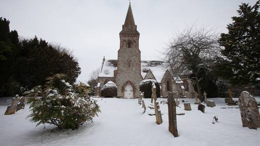 A snow-covered church with a tall spire and a graveyard with headstones.