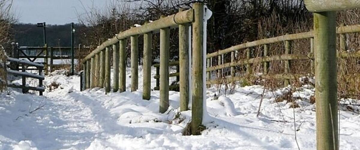 A snow-covered path with wooden posts and a wooden fence.
