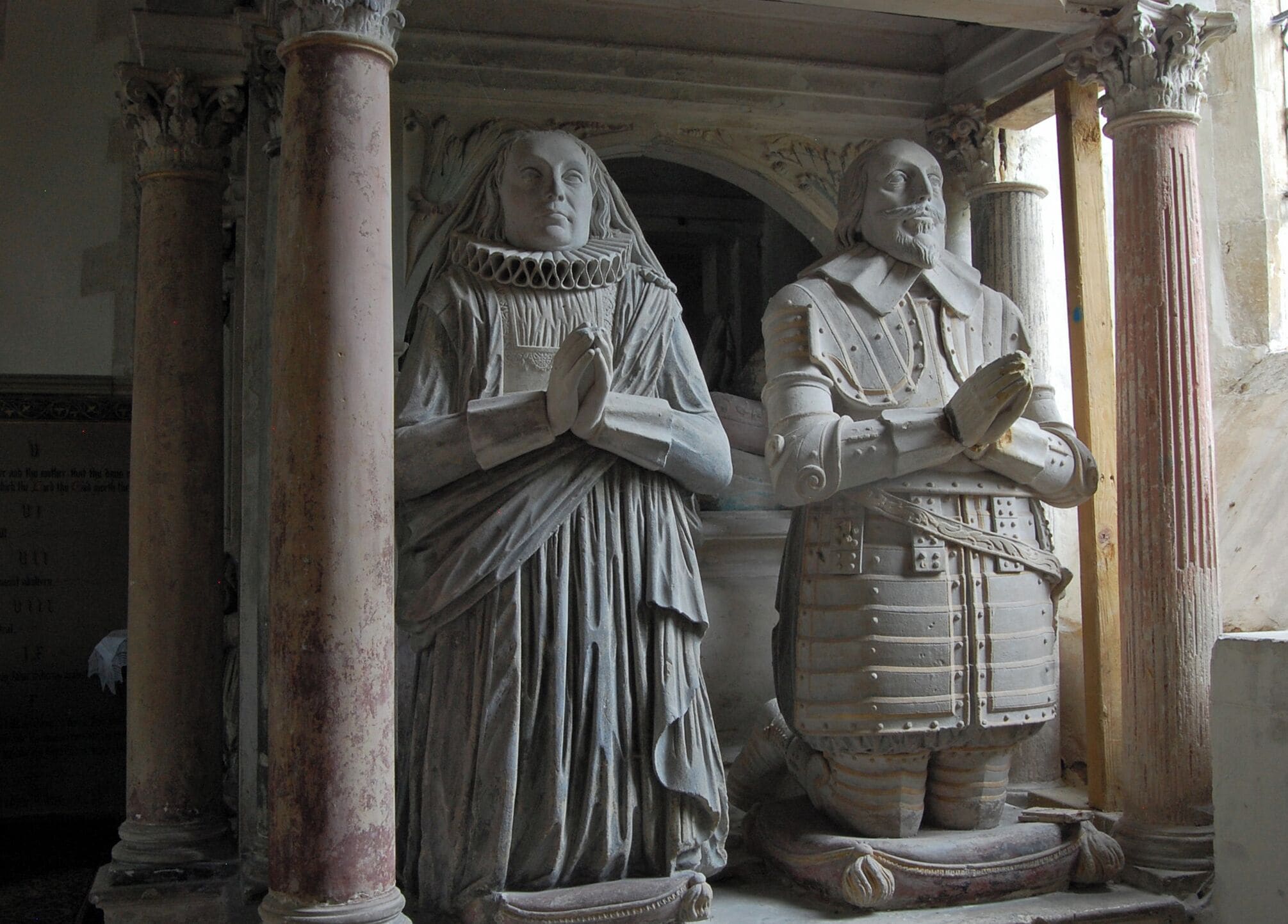 A statue of a woman in a long dress and a man in armor, both standing in a stone archway with columns.