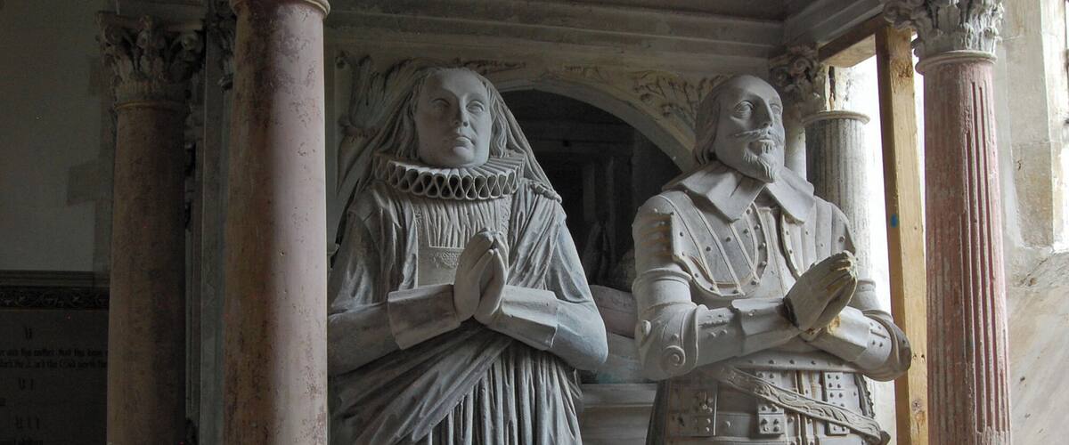 A statue of a woman in a long dress and a man in armor, both standing in a stone archway with columns.