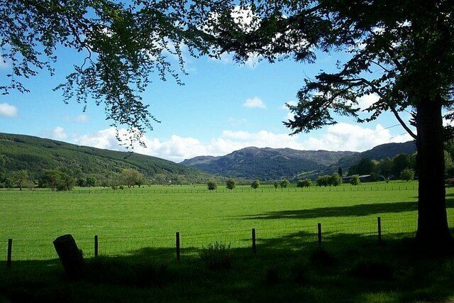 A green field with a fence, trees, and hills in the background.
