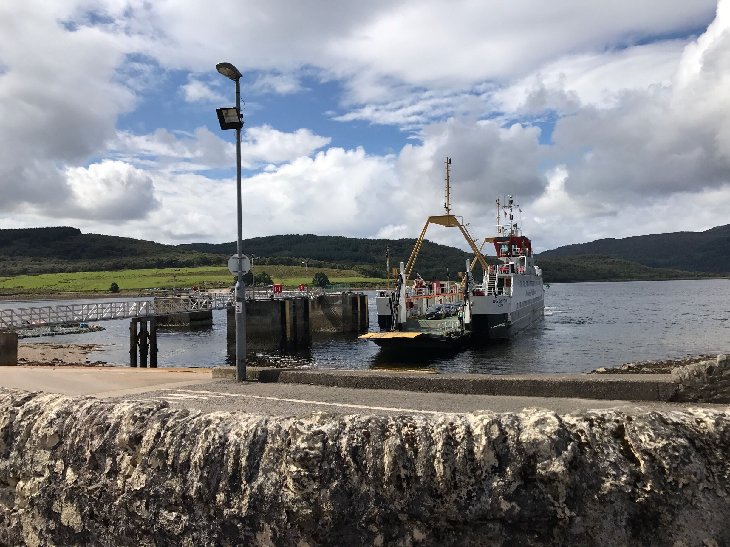 A ferry docked at a pier with a bridge in the background and hills in the distance.
