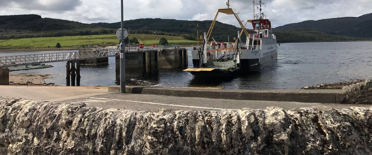 A ferry docked at a pier with a bridge in the background and hills in the distance.