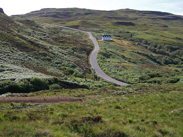 Road to Glendale The single track road climbs out of Colbost, viewed here from just west of Dùn Colbost. The building is the old school house, now a craft shop.