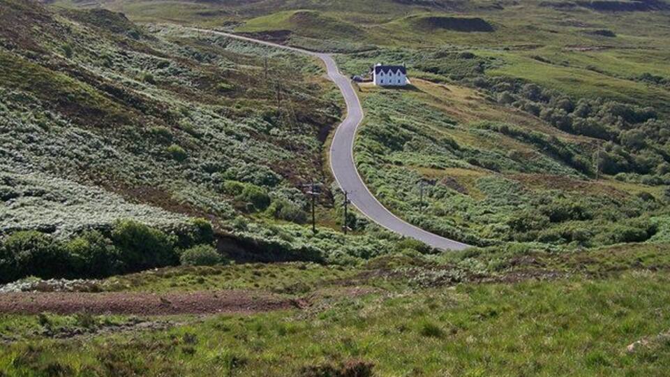 Road to Glendale The single track road climbs out of Colbost, viewed here from just west of Dùn Colbost. The building is the old school house, now a craft shop.