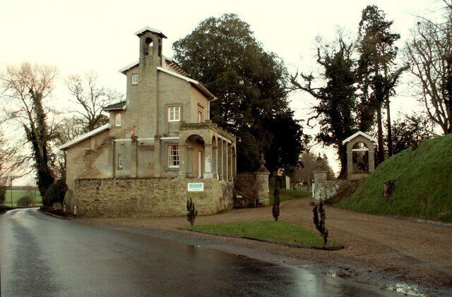 A stone building with a bell tower, a small church, and a grassy hill in the background.