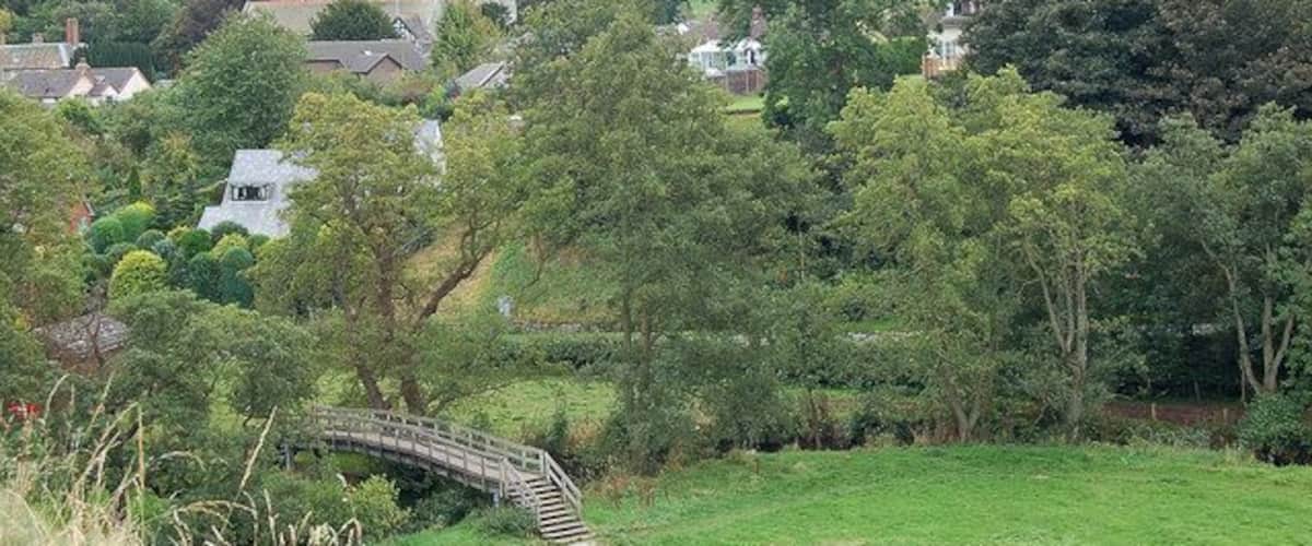 A rural landscape with a bridge, trees, and houses in the background.