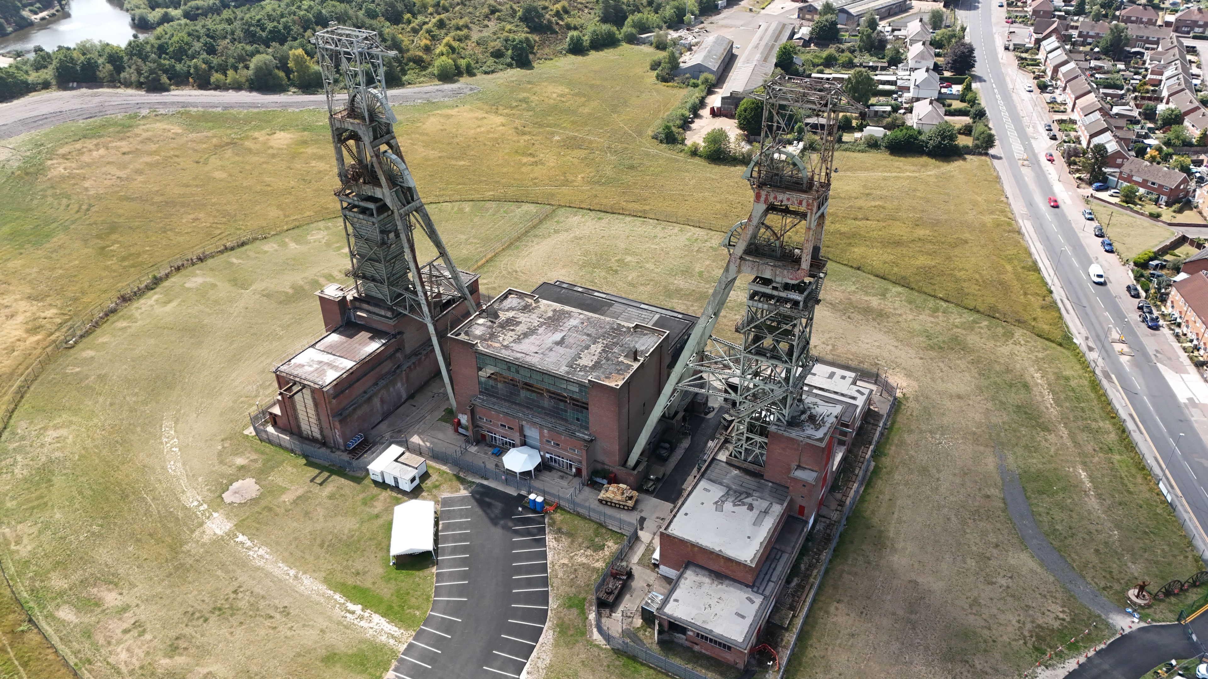 Un complejo industrial con grandes estructuras metálicas, una carretera y edificios residenciales al fondo.