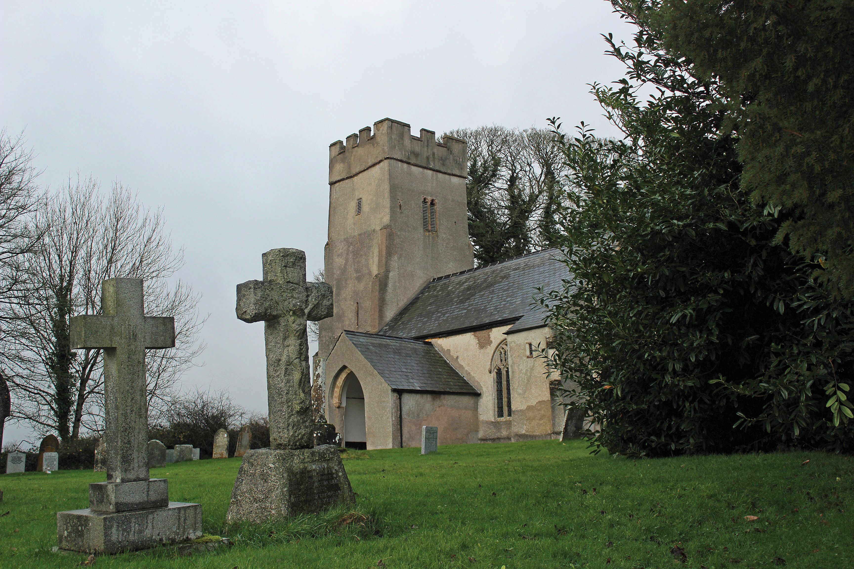 A church with a tall tower and a large stone cross in a cemetery.