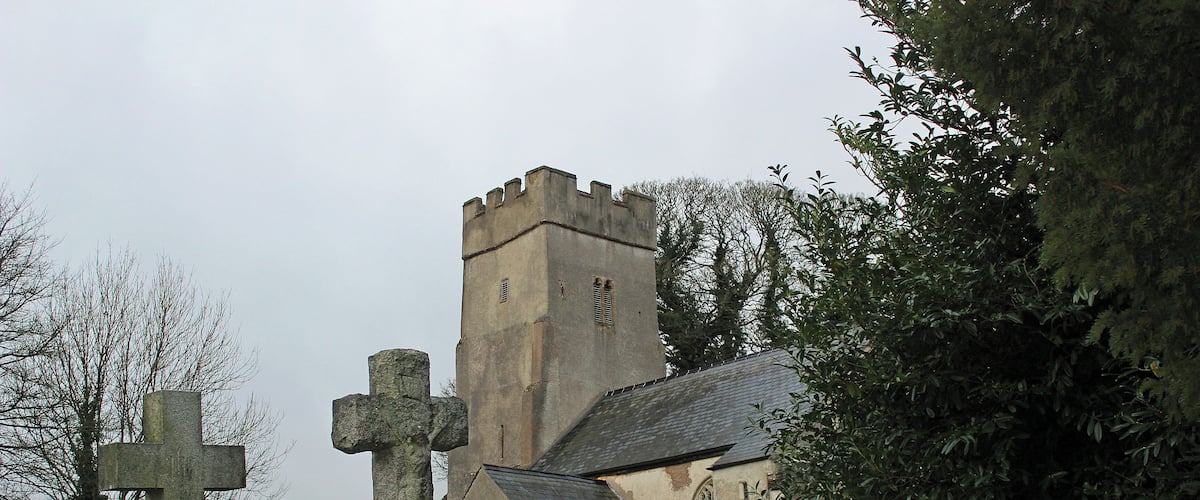 A church with a tall tower and a large stone cross in a cemetery.