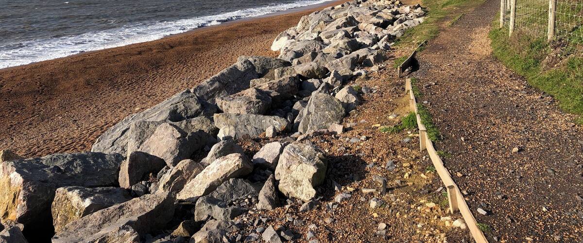 A rocky beach with waves crashing onto the shore, a grassy path, and a cliff in the background.