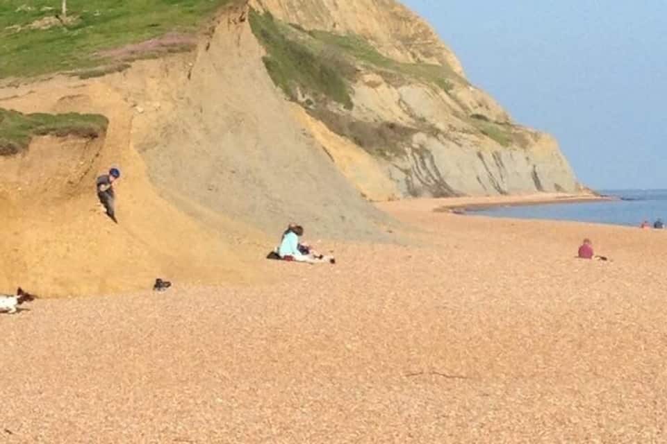 Une plage de galets où des gens se prélassent au soleil, avec une falaise en arrière-plan.
