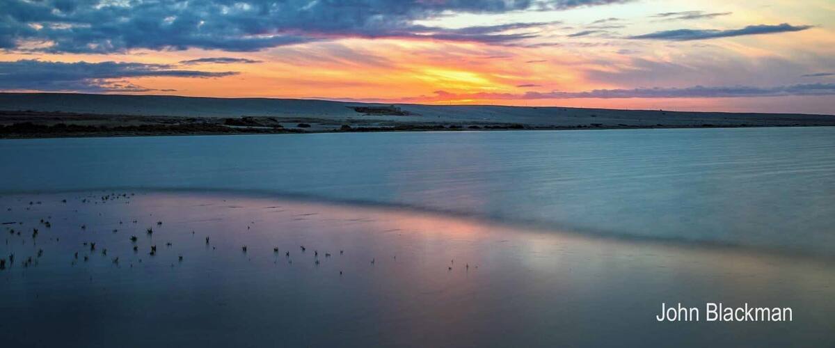 A sunset over a calm sea with a cloudy sky.