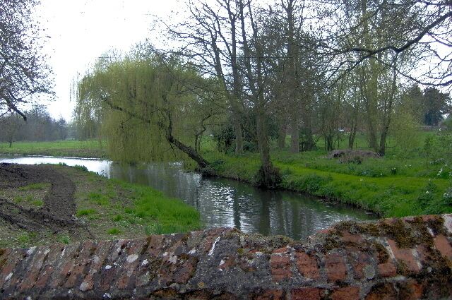 A river flowing through a park with trees and a brick wall in the foreground.