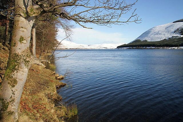 A calm lake with snow-capped mountains in the background.
