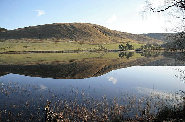 A calm lake reflecting hills and a clear sky.