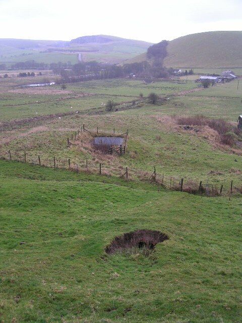 Mining remains, Rushup Farm. In the foreground is a collapsed brick flue, and behind that (covered by a square grille and enclosed within a fence) a disused mineshaft. On Gautries Hill behind the position of a "rake" (a line of lead mines along a vein of ore) is indicated by the line of trees. Eldon Hill Quarry is in the distance to the left of this picture.
