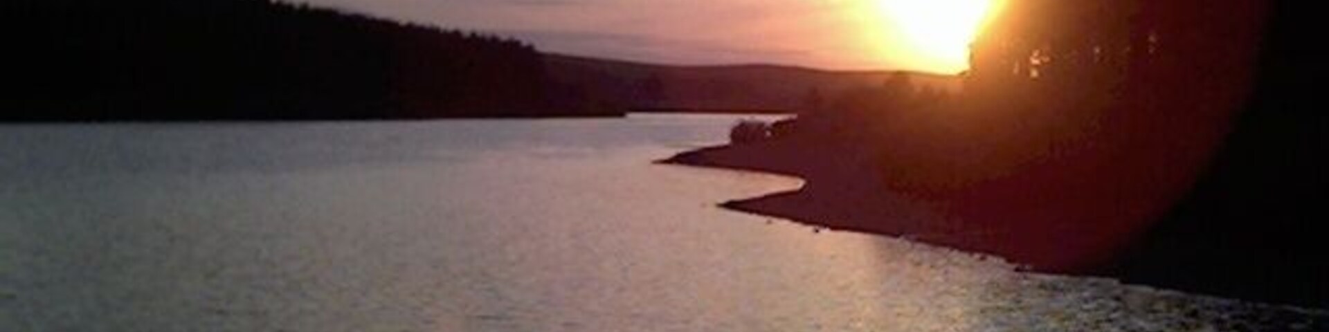 Un atardecer sobre un lago tranquilo con una orilla arbolada.