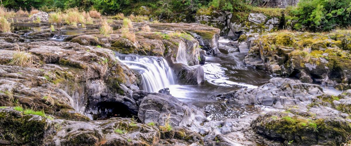 A waterfall cascading over rocky terrain with a stone building in the background.