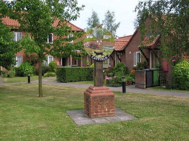A brick monument with a plaque in a grassy area with houses in the background.
