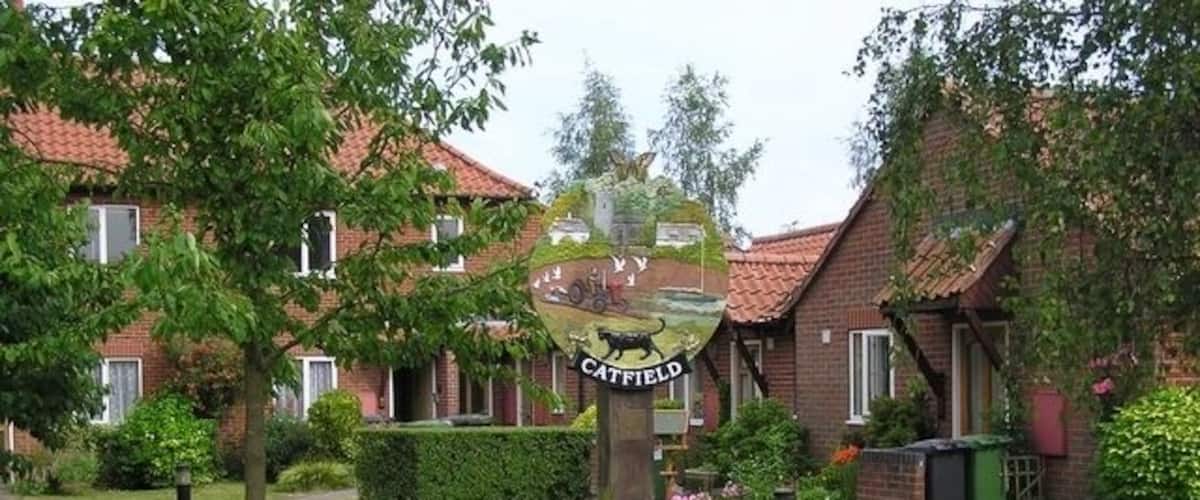 A brick monument with a plaque in a grassy area with houses in the background.