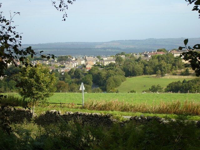 A rural landscape with a stone wall, a triangular warning sign, and a village in the distance.