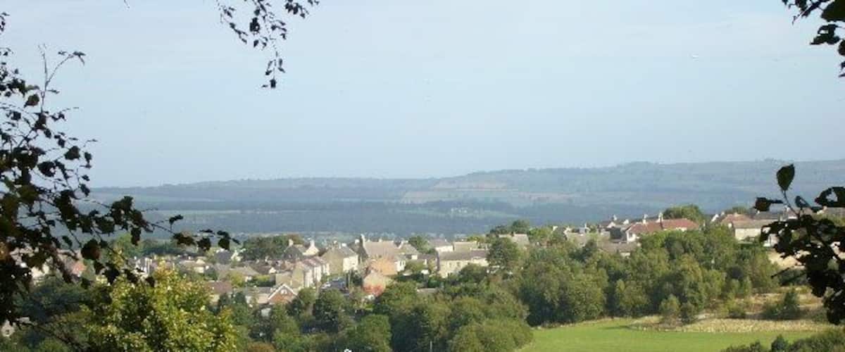 A rural landscape with a stone wall, a triangular warning sign, and a village in the distance.