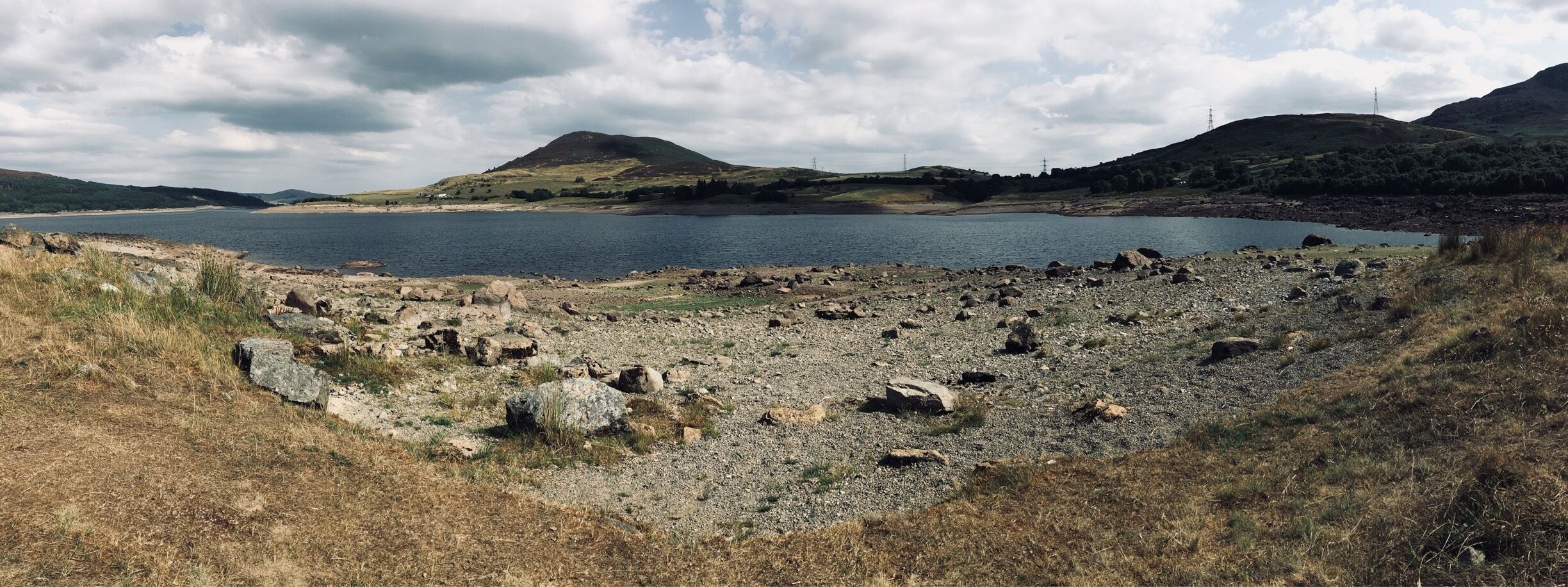 Llyn Celyn Resevoir, Snowdonia North Wales. Water lever extremely low due to our dry spell in the UK. 
lyn Celyn is a large reservoir constructed between 1960 and 1965 in the valley of the River Tryweryn in Gwynedd, Wales. It measures roughly 2.5 miles long by 1 mile wide, and has a maximum depth of 140 ft.