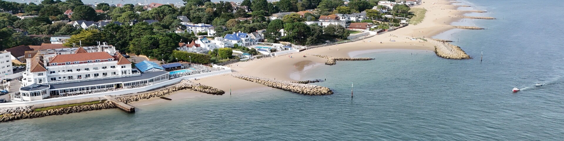 Un pueblo costero con puerto deportivo, playa de arena y rompeolas rocosas.