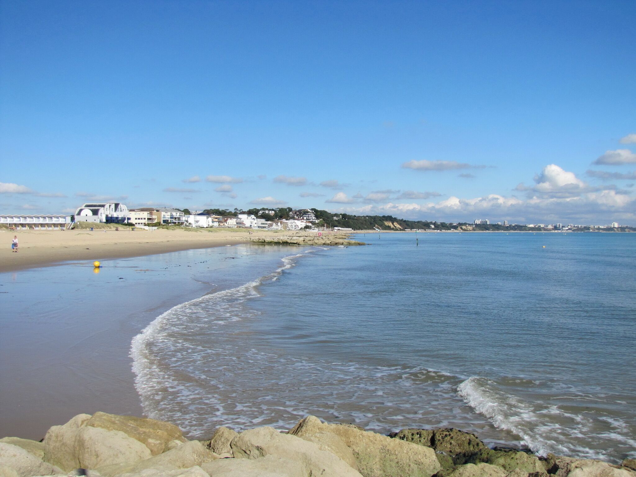 A beach with waves, a sandy shore, and buildings in the background.