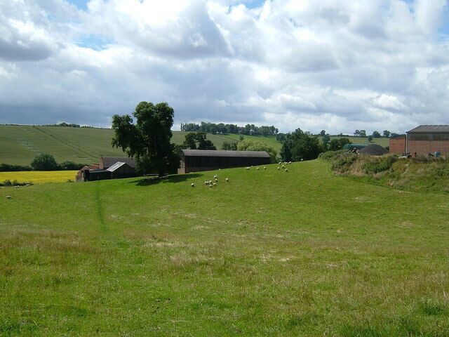 A rural landscape with a barn, sheep, and rolling green fields under a partly cloudy sky.
