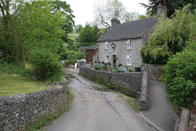 A narrow stone-lined road in a rural area with stone walls and greenery.