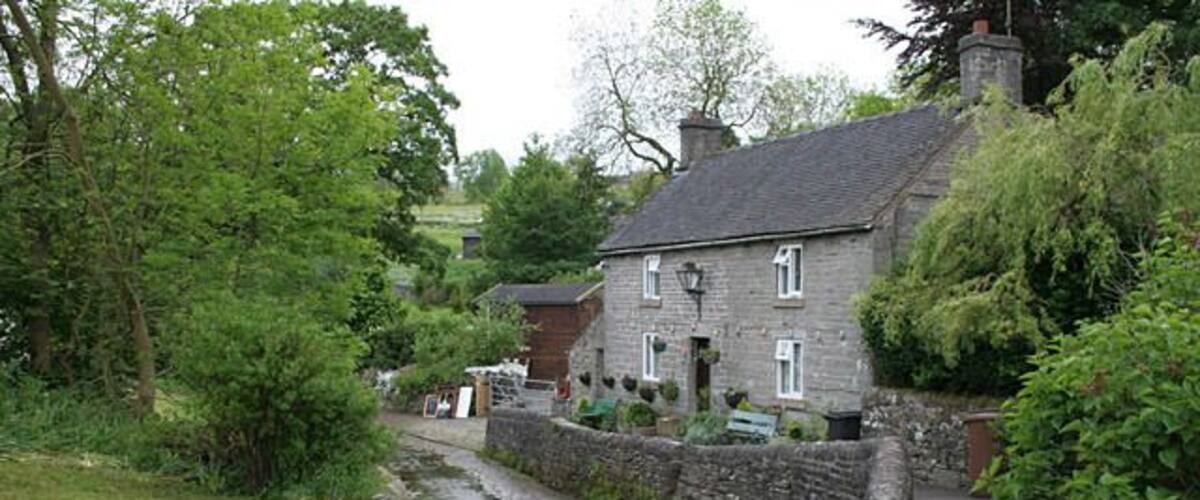 A narrow stone-lined road in a rural area with stone walls and greenery.