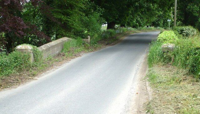 A narrow rural road flanked by stone walls and dense greenery.