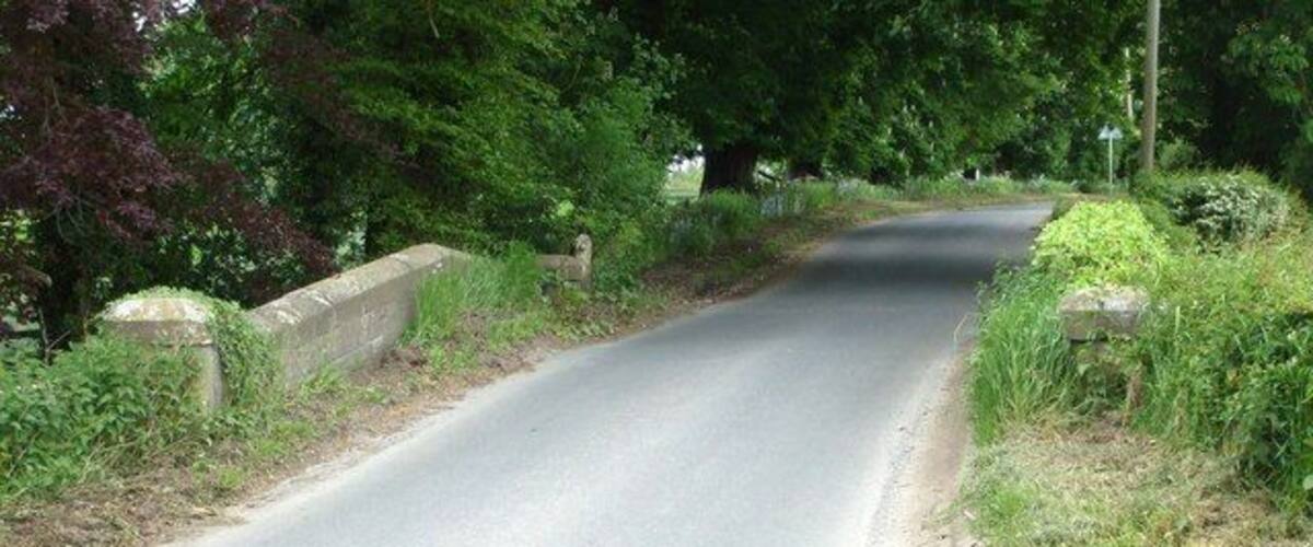 A narrow rural road flanked by stone walls and dense greenery.