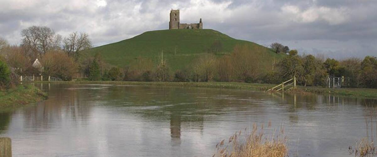 Un lago tranquilo con un castillo en una colina, rodeado de árboles y un cielo nublado.