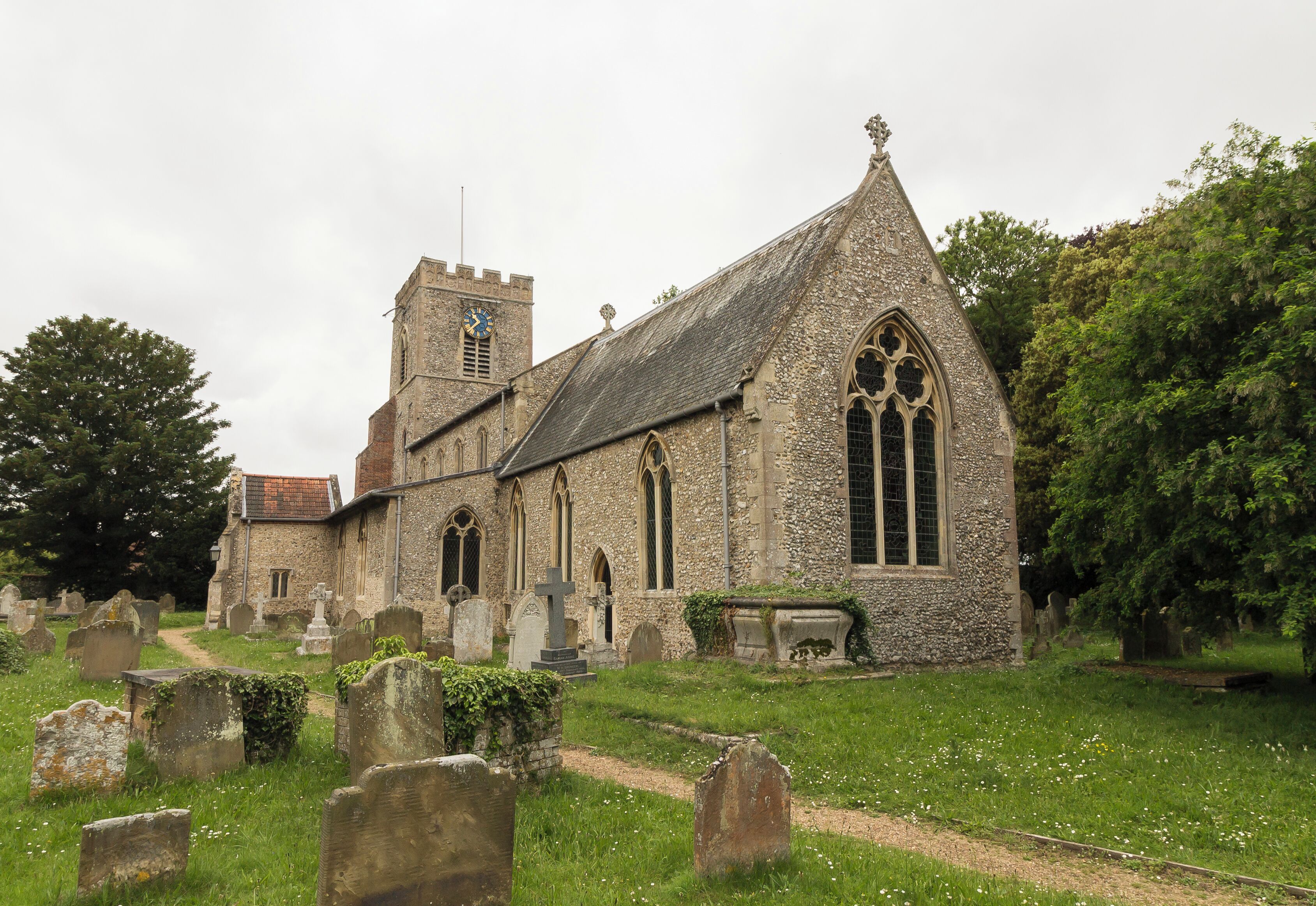 A historic church with a clock tower, surrounded by a cemetery with headstones and a grassy path.
