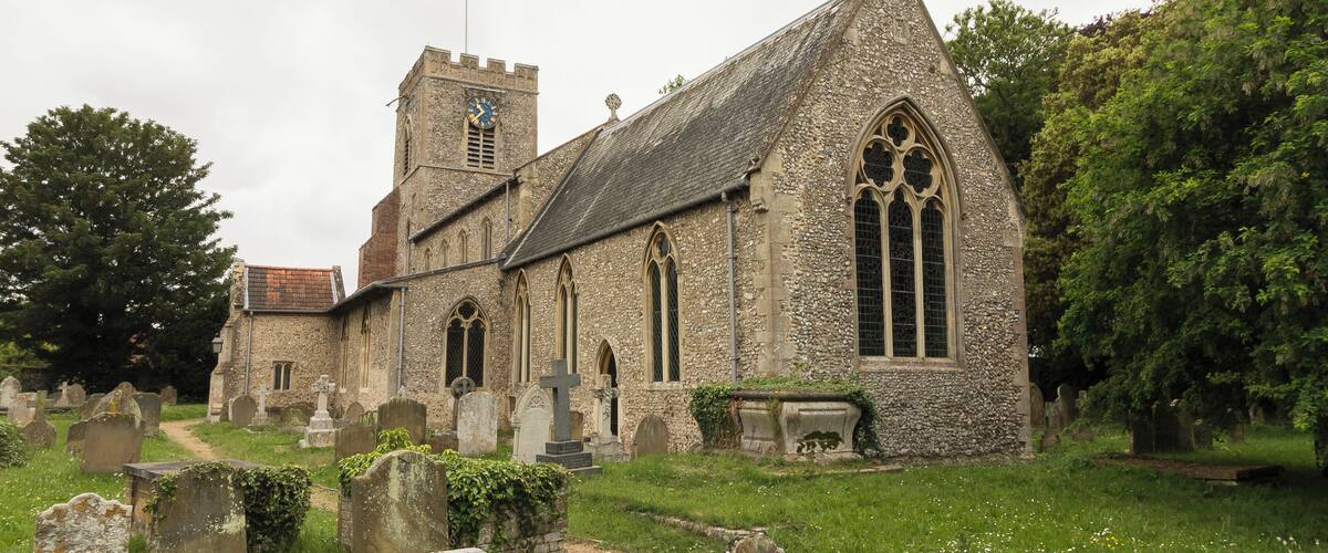 A historic church with a clock tower, surrounded by a cemetery with headstones and a grassy path.