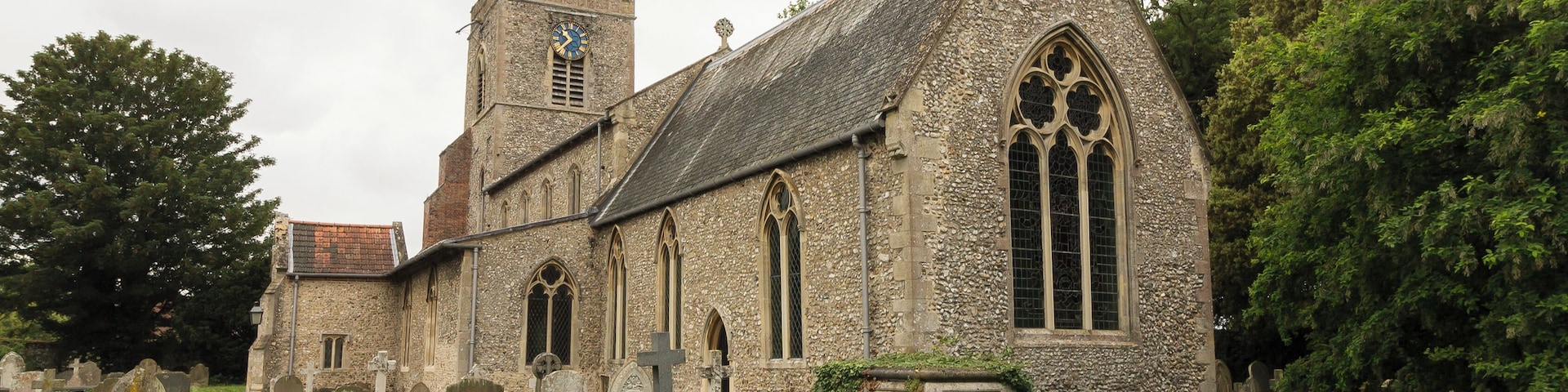 A historic church with a clock tower, surrounded by a cemetery with headstones and a grassy path.