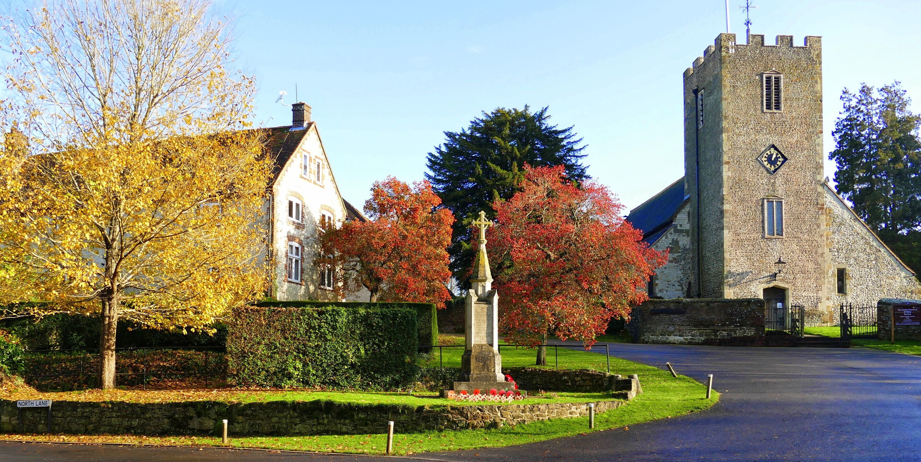 A historic stone tower, a church, and a residential building with autumn foliage.