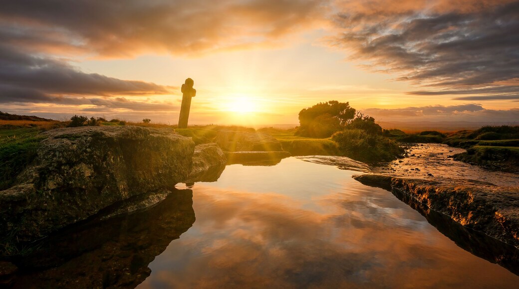 A sunset over a rocky landscape with a person standing on a rock.