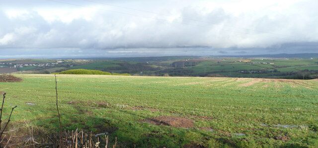 A rural landscape with rolling hills, a field, and a distant village.