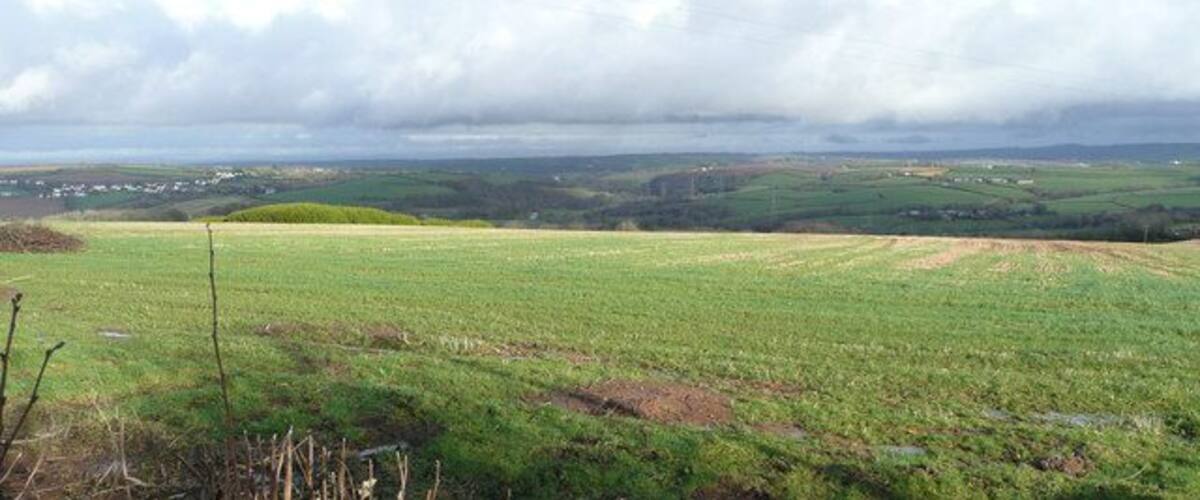 A rural landscape with rolling hills, a field, and a distant village.